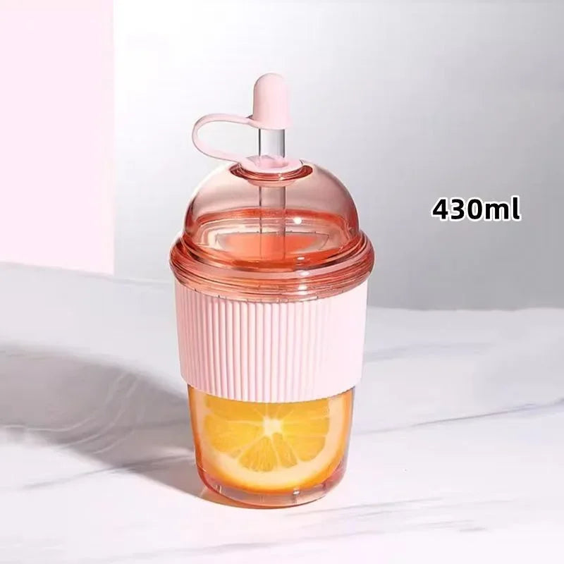 Klares Glas mit Orangensaft, rosa Deckel und Strohhalm, auf weißer Oberfläche.
