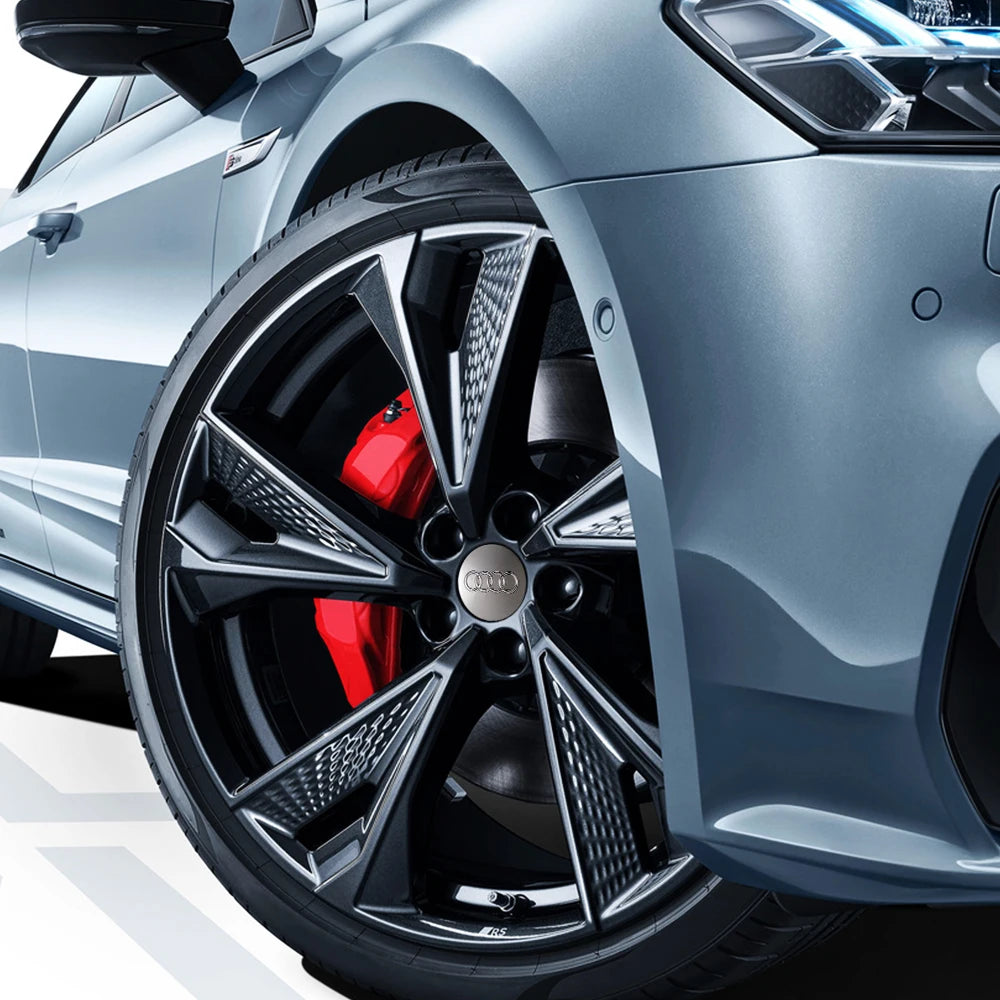 Close-up of a silver Audi wheel with black decorative hub caps and red brake calipers.