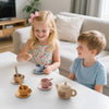 A young girl and boy are playing with a bear silicone pretend play teapot set on a white table.