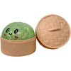 Rundes, grünes Glitzer-Squishy Spielzeug mit lächelndem Gesicht neben seinem geöffneten, beigen Deckel.