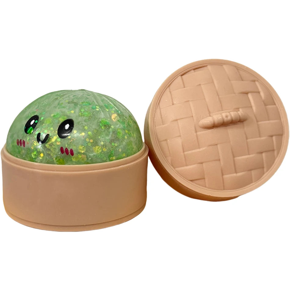 Rundes, grünes Glitzer-Squishy Spielzeug mit lächelndem Gesicht neben seinem geöffneten, beigen Deckel.