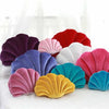 A collection of decorative velvet shell print throw pillows in shades of purple, pink, red, white, and blue arranged on a whi
