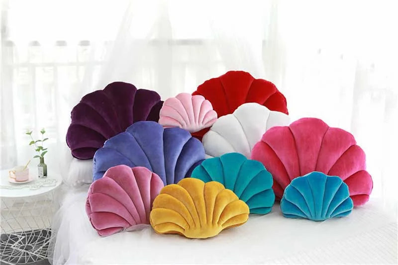 A collection of decorative velvet shell print throw pillows in shades of purple, pink, red, white, and blue arranged on a whi