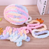 A ball of multi-colored chenille yarn with pink, purple, and blue swirls lying next to a knitted scarf.