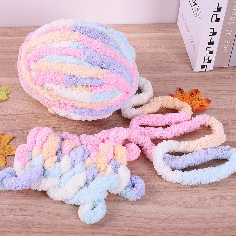 A ball of multi-colored chenille yarn with pink, purple, and blue swirls lying next to a knitted scarf.