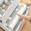 A roll of daisy flower waterproof kitchen drawer mats is being placed into a white organizer tray.