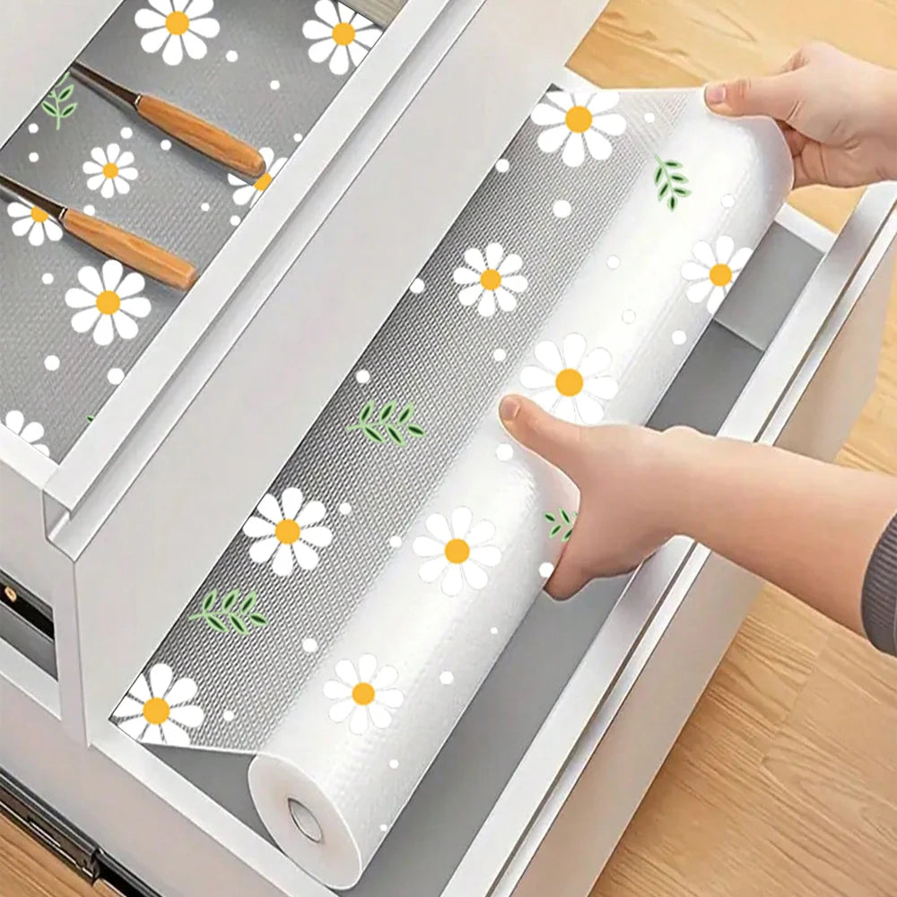 A roll of daisy flower waterproof kitchen drawer mats is being placed into a white organizer tray.