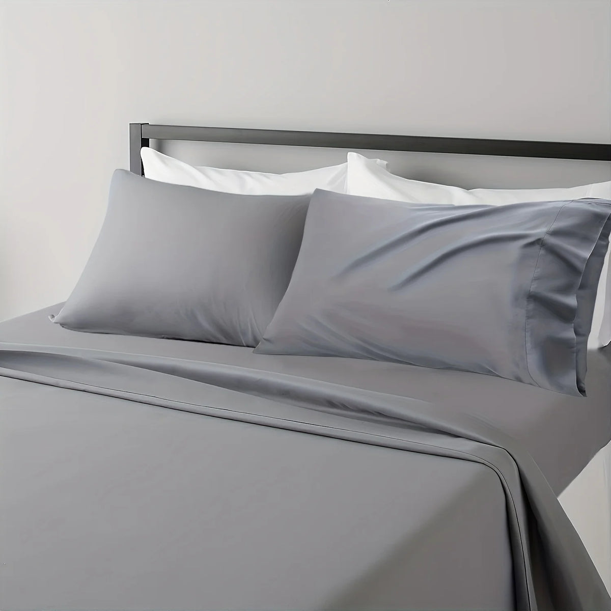 A gray microfiber bed sheet set with white linens is displayed on a bed with a dark headboard.