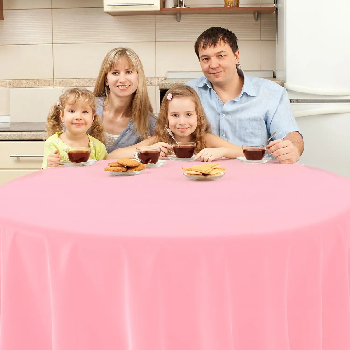 A family of four enjoying a meal around a pink round table in a kitchen setting.