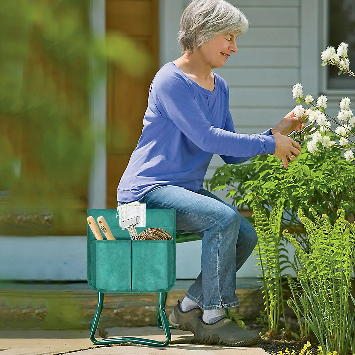 An elderly woman in a blue shirt sits on a green foldable garden kneeler seat, tending to plants outdoors.