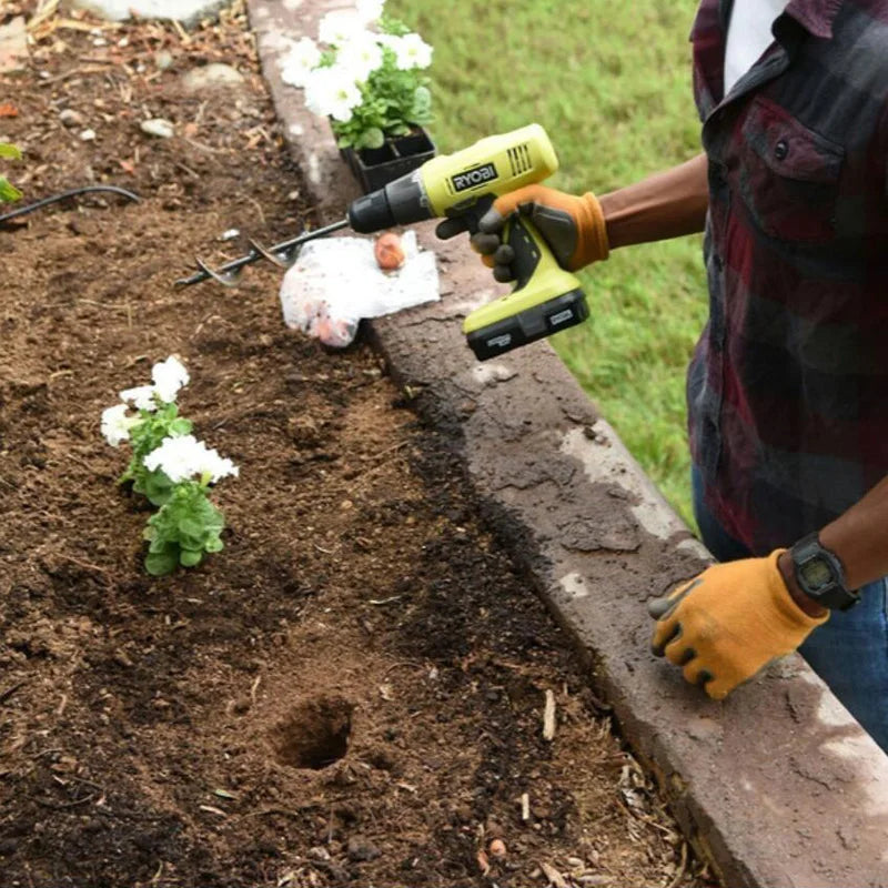 A person uses a yellow garden auger drill to create a hole in the soil for planting.