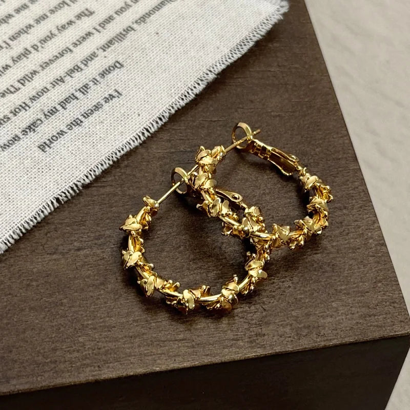 A pair of twisted zircon hoop earrings in a gold finish resting on dark brown paper.
