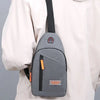 A gray Oxford canvas crossbody chest bag with a black strap and orange accents is shown against a light-colored shirt.