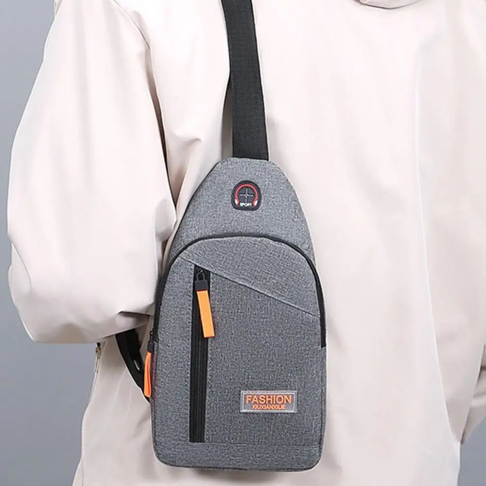 A gray Oxford canvas crossbody chest bag with a black strap and orange accents is shown against a light-colored shirt.