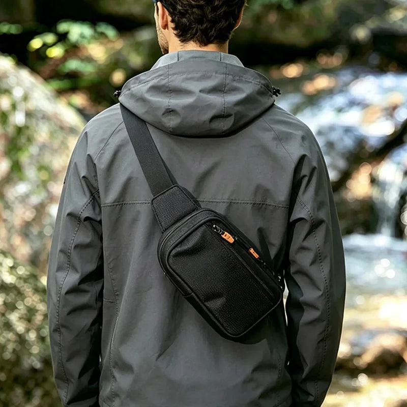 A person wearing a gray jacket is shown from the back, carrying a black sling bag on their shoulder in an outdoor setting.