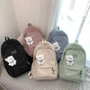 A collection of pastel-colored backpacks featuring white teddy bear designs displayed on a striped surface.