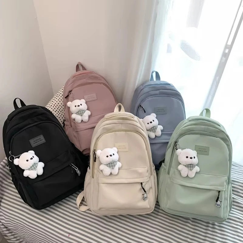 A collection of pastel-colored backpacks featuring white teddy bear designs displayed on a striped surface.