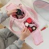 A hand is opening a pink travel makeup bag revealing various cosmetic products on a white surface.