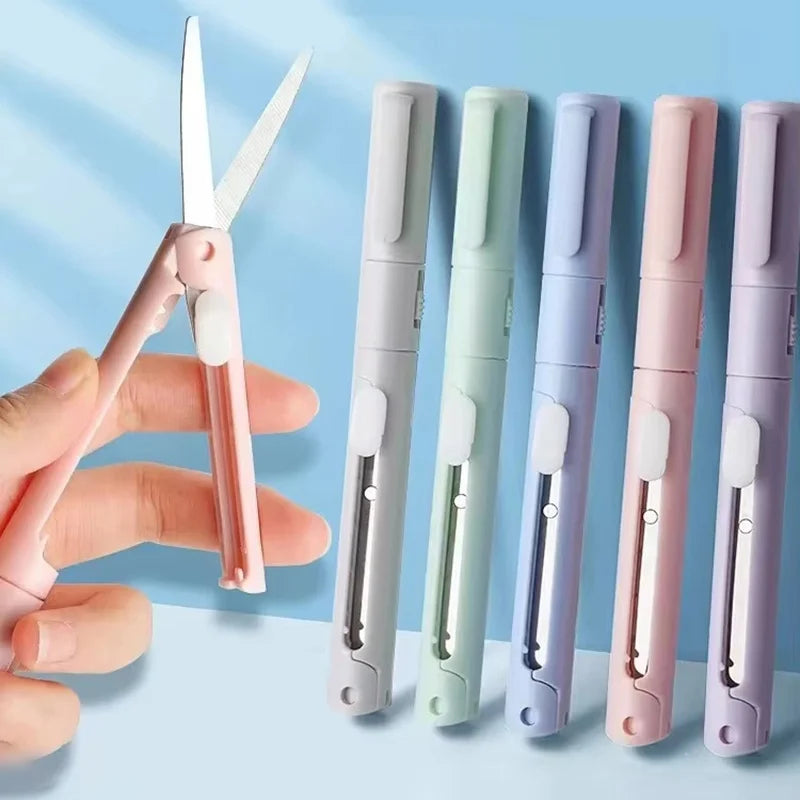 A hand holds a pink folding pen-shaped safety scissor with multiple color options.