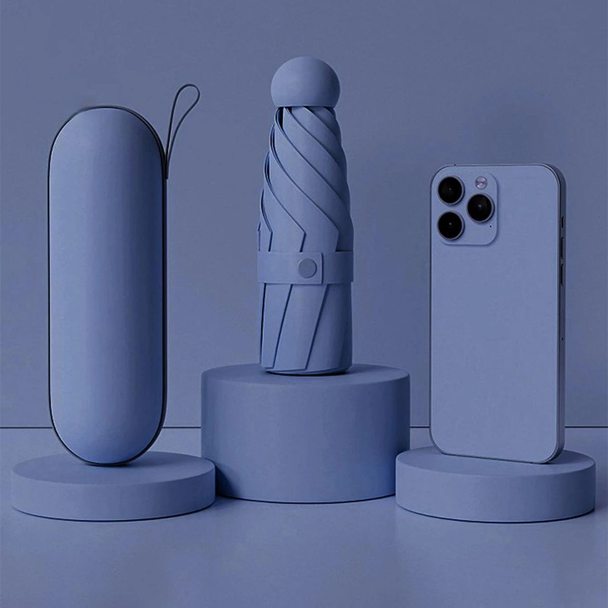 A light blue compact folding umbrella is displayed next to a smartphone and a cylindrical accessory on a surface.