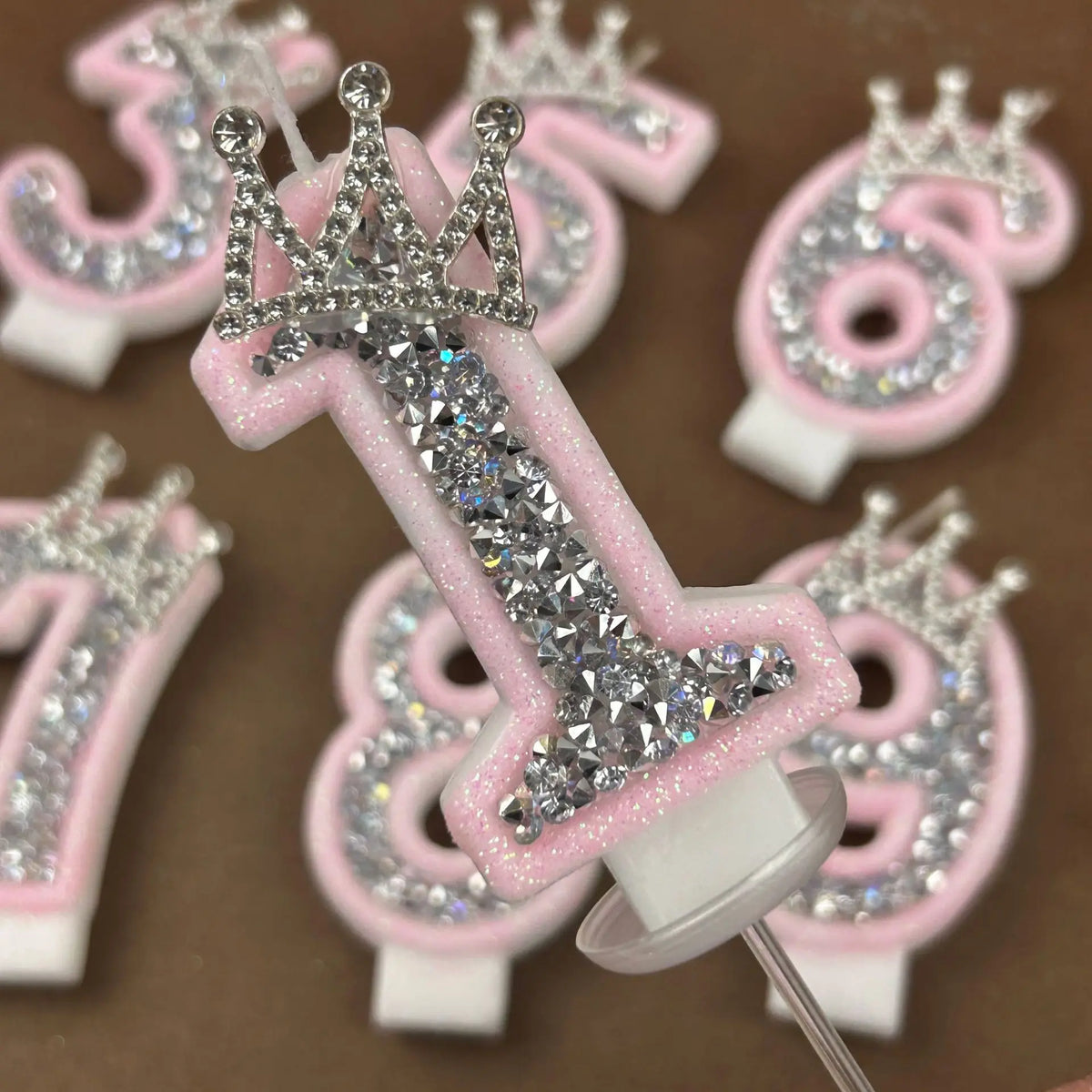 A collection of pink and white rhinestone crown number candles for birthday cakes, including the numbers 3, 6, and 9.