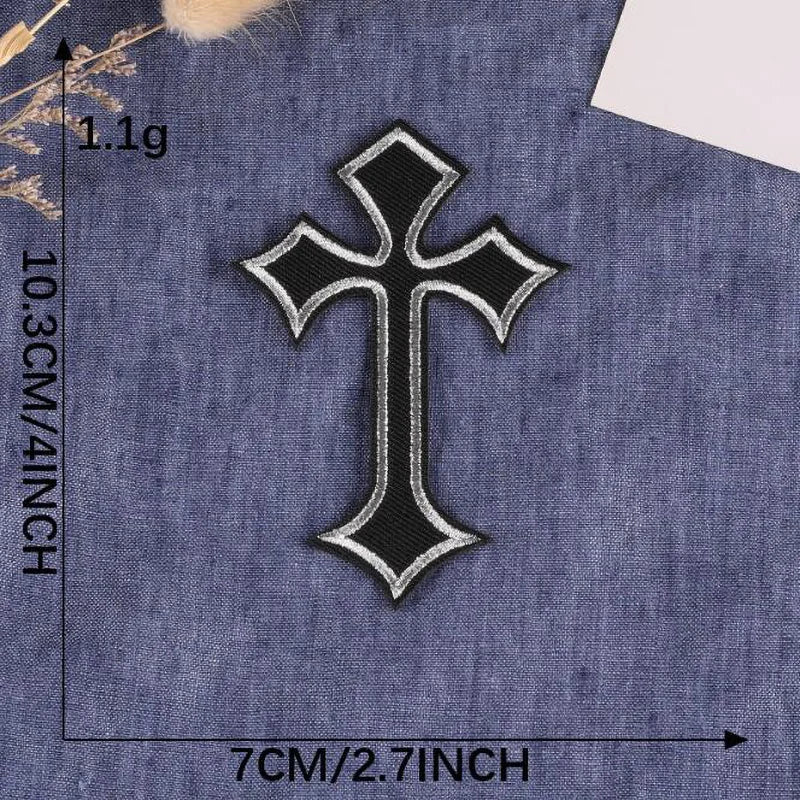 A black embroidered cross patch on a dark blue denim fabric.