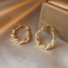 A pair of gold-finished twisted zircon hoop earrings resting on a beige fabric surface.