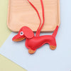 A red dachshund puppy keychain made of PU leather lying on a light wooden cutting board.
