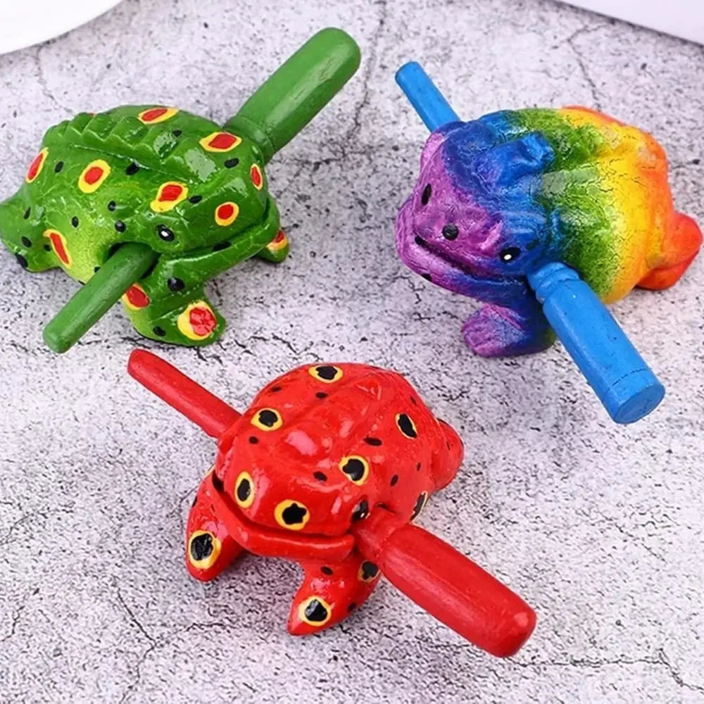Three handcrafted wooden frog guiro rasp percussion instruments in green, purple, and red.