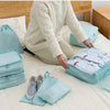 A person is organizing a set of light blue travel packing cubes and storage bags on a bed.