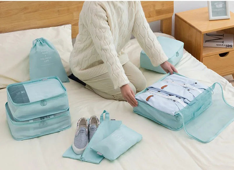 A person is organizing a set of light blue travel packing cubes and storage bags on a bed.