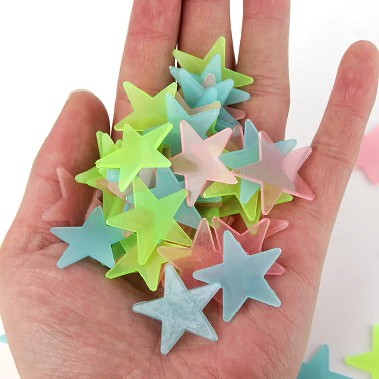A hand holds a collection of 100 luminous star-shaped wall stickers in various pastel colors like green, blue, and pink.