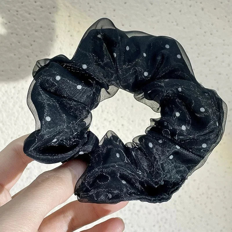 A hand holds a black polka dot mesh scrunchie hair tie, showing its soft and breathable texture.