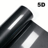 Glossy black carbon fiber vinyl wrap film rolled up, showing a textured surface and a reflective sheen.