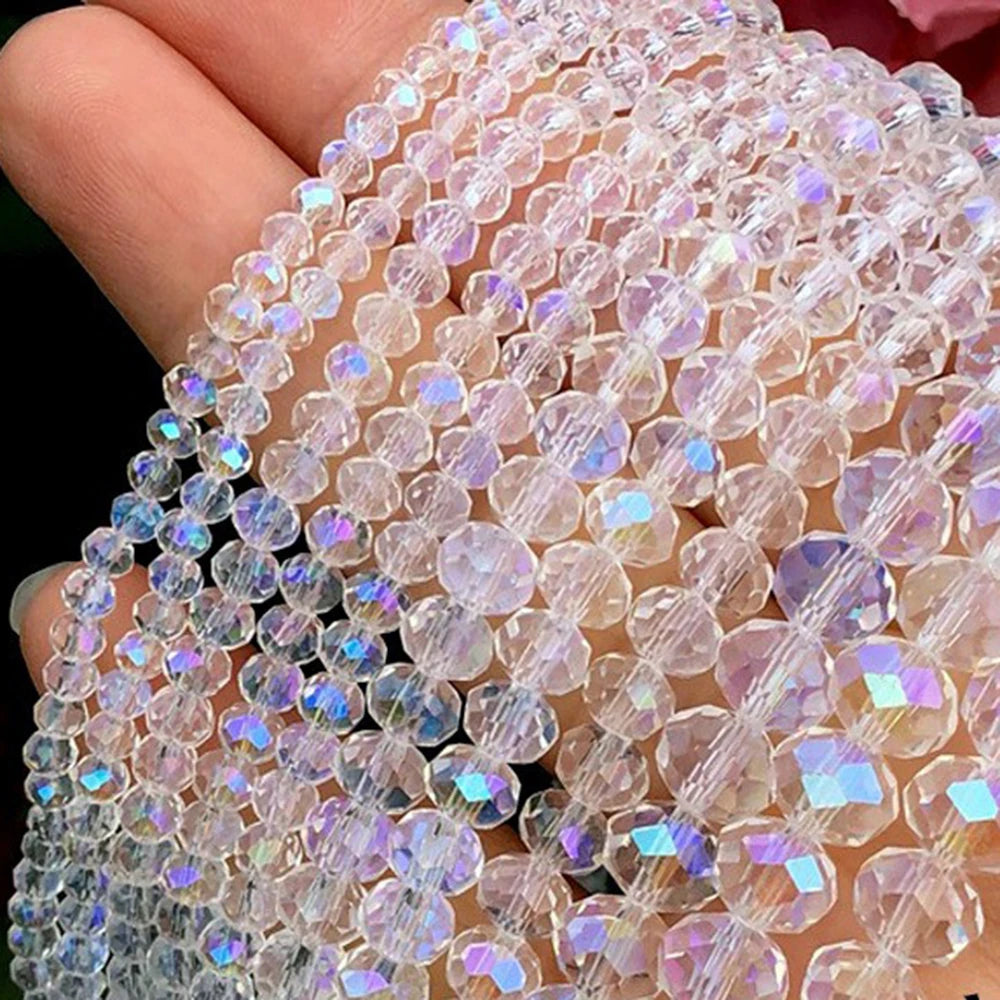 A hand holds a strand of clear pink faceted crystal glass spacer beads for jewelry making.