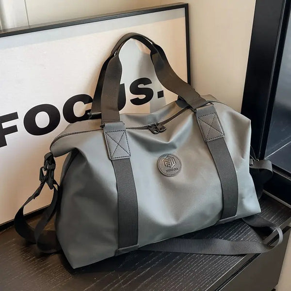 A gray travel duffel bag with black straps is displayed in front of a framed sign.