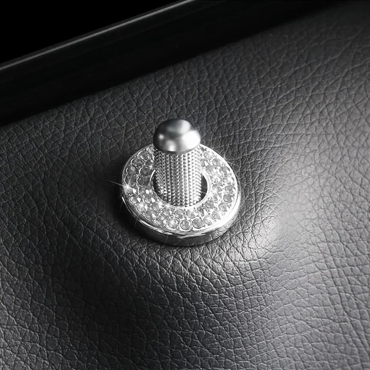 Close-up black leather surface showing a silver crystal rhinestone car door lock pull cover.