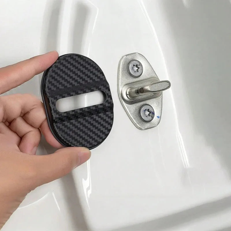 A hand holds a black carbon-fiber door lock cover and a silver door lock mechanism against a white surface.