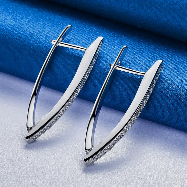 Pair of silver V-shaped hoop earrings with zircon accents displayed on a blue velvet fabric.