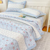 A light blue and white floral quilted bedspread with pink flowers is displayed on a bed.