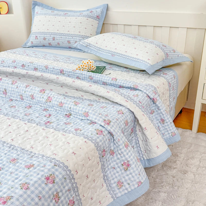 A light blue and white floral quilted bedspread with pink flowers is displayed on a bed.
