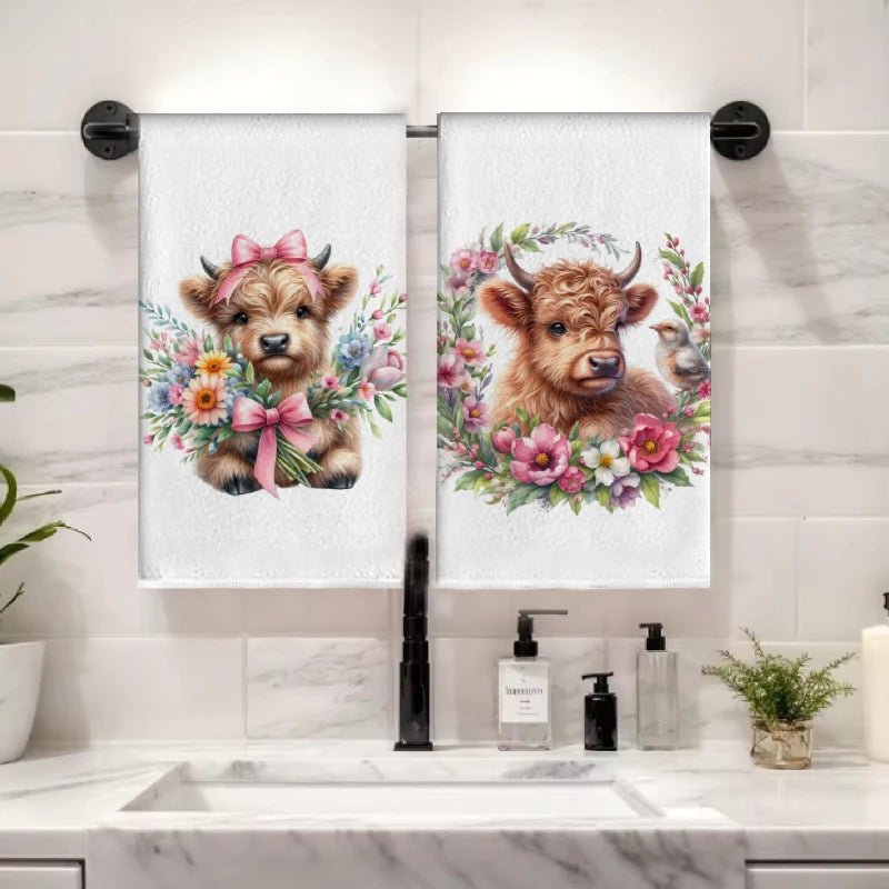 A set of two white kitchen towels featuring a watercolor illustration of a cute Highland cow's head with pink flowers.