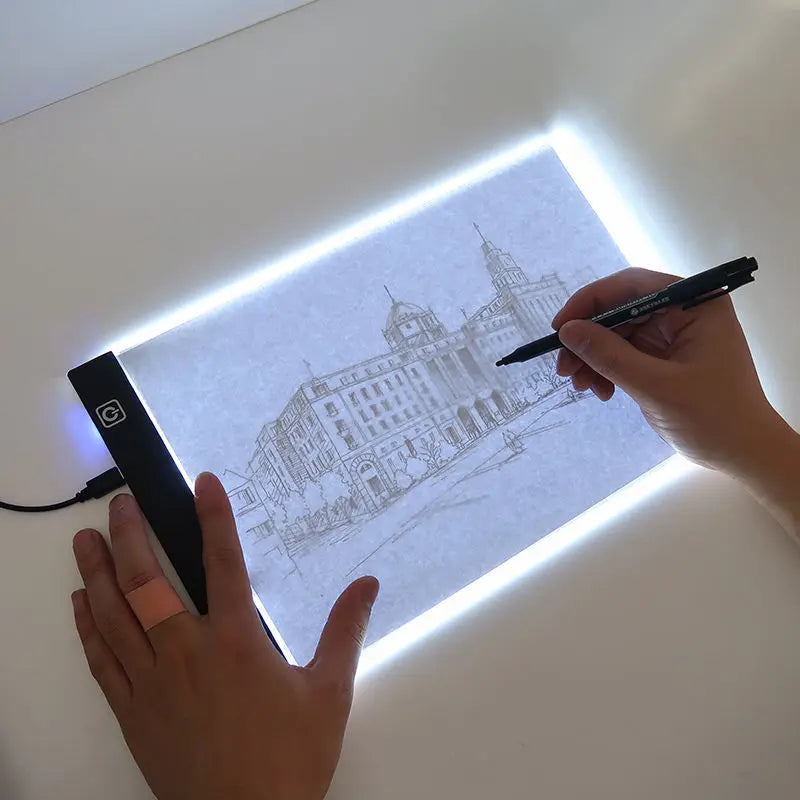 A hand draws a detailed outline of a building on a transparent LED tracing light with a pen.