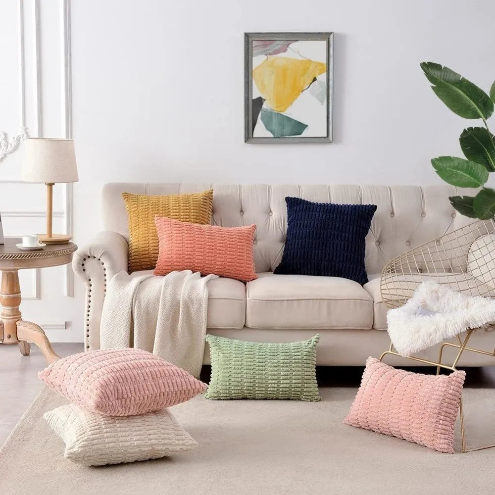 A collection of pink, yellow, green, and purple corduroy and velvet pillows arranged on a light-colored sofa and floor.