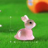 A pink resin miniature bunny figurine sitting on green grass.