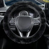 Close-up view of a black steering wheel with a fuzzy black cover inside a car interior.
