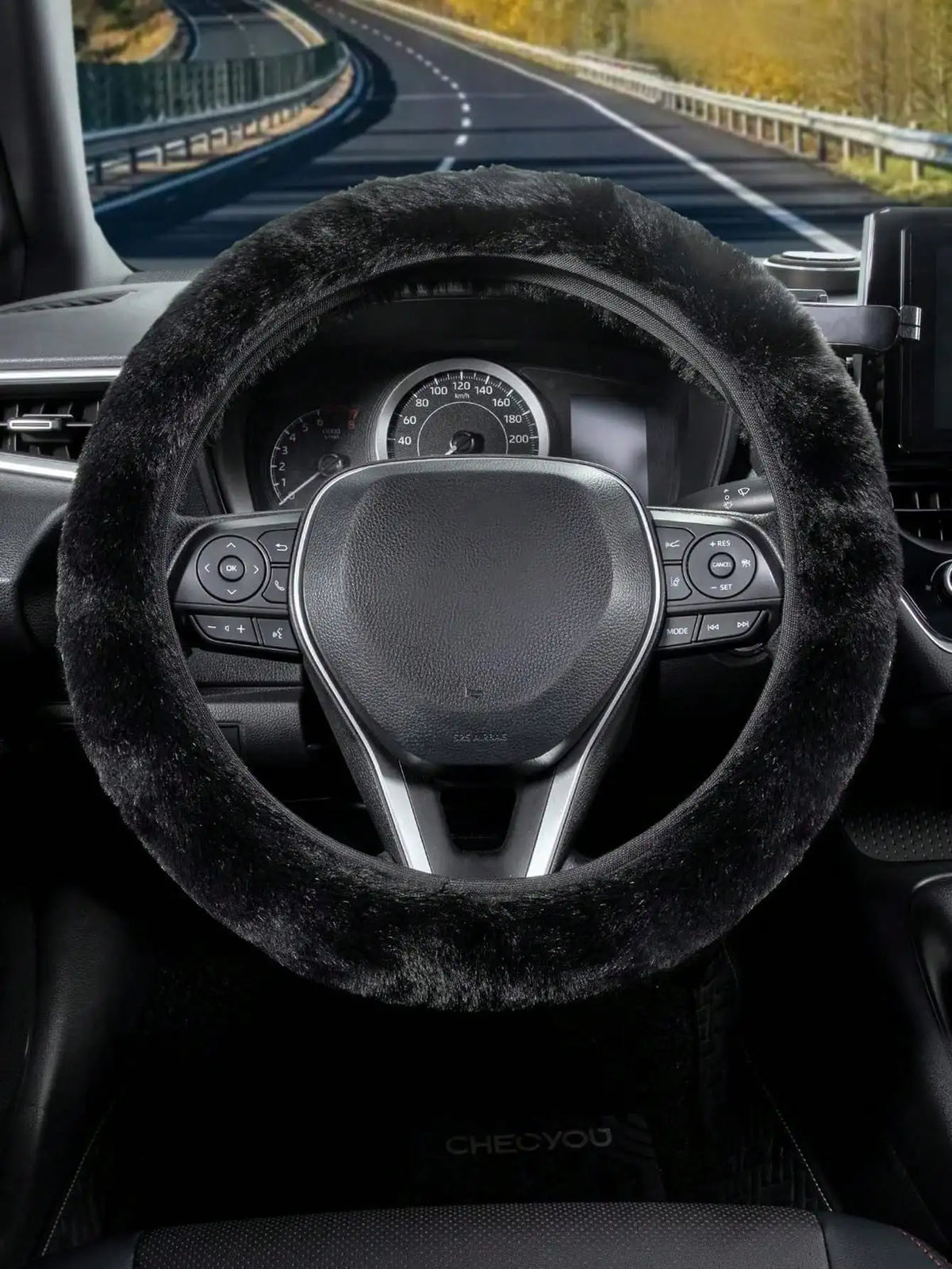 Close-up view of a black steering wheel with a fuzzy black cover inside a car interior.