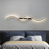 A modern minimalist LED wall lamp with a curved, illuminated light fixture mounted above a bed.
