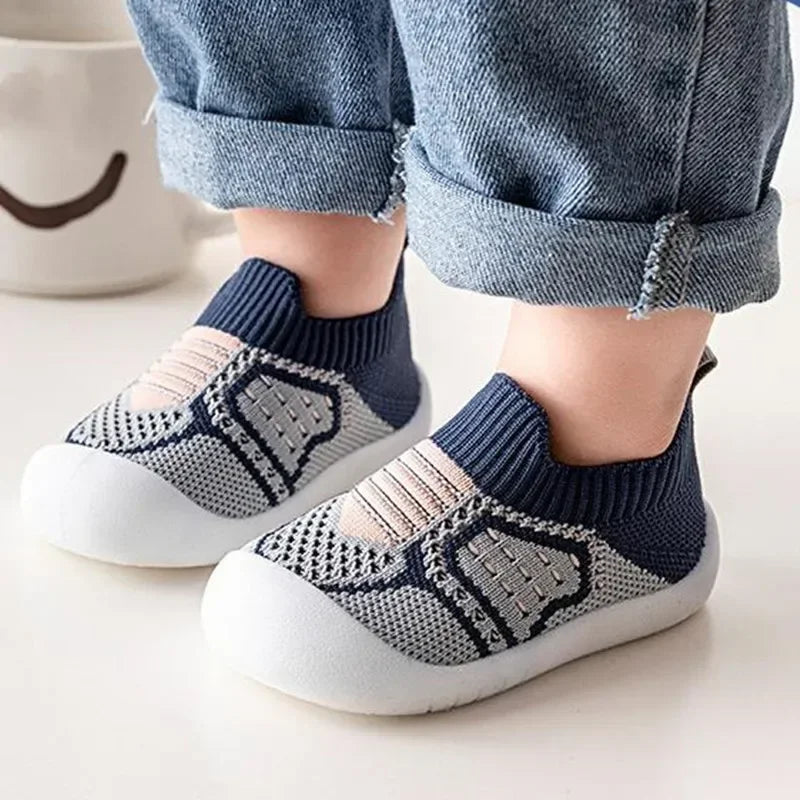 A pair of navy blue and beige breathable soft-sole baby shoes with non-slip grip shown on a person's foot.