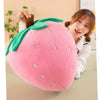 A pink strawberry plush throw pillow with green leaves is being held by a woman.